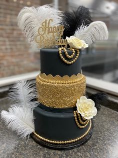 a three tiered black and gold cake with feathers