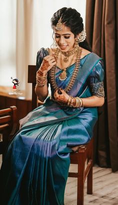 a woman sitting on top of a wooden chair wearing a blue sari and jewelry