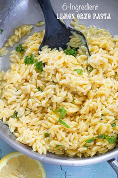 lemon orzo pasta in a skillet with a spoon and lemon slices on the side