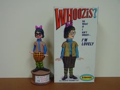 an old toy doll next to a box on a wooden table with a sign that says whoozies?