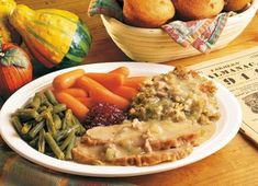 a white plate topped with meat covered in gravy next to veggies and muffins