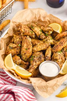 chicken wings with lemon wedges and ranch dressing in a bowl on a table next to french fries