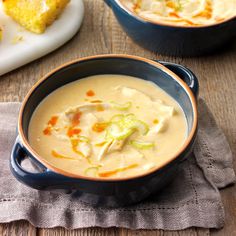 two blue bowls filled with soup on top of a wooden table next to cornbreads