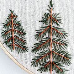 two embroidered pine trees sitting next to each other on a piece of white fabric with orange thread