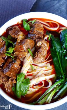 a white bowl filled with meat and noodles next to green leafy garnish