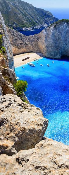 the blue water is surrounded by rocky cliffs and boats in the bay at the end of the cliff