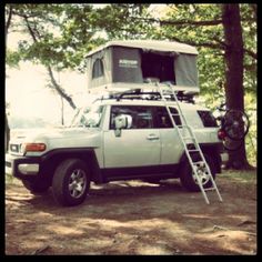 a truck with a ladder attached to it parked in the woods next to a camper