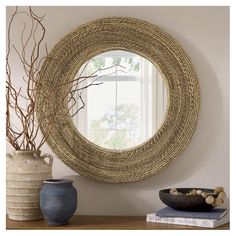 a round mirror sitting on top of a wooden table next to a vase filled with branches