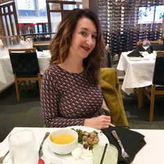 a woman sitting at a table in front of a plate of food and wine glasses