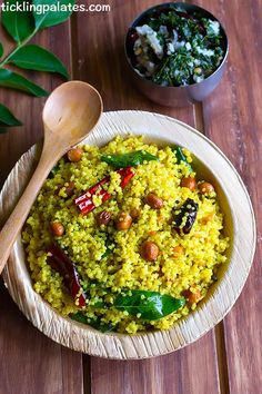 a bowl filled with rice and vegetables next to a wooden spoon on top of a table