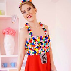 a woman in a red dress is holding a bag and wearing a necklace with colorful balls on it