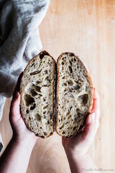 a person holding a piece of bread in their hands on top of a wooden table