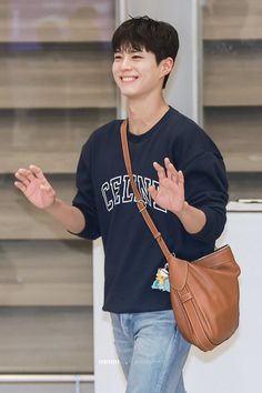 a young man carrying a brown handbag and waving to someone in front of him