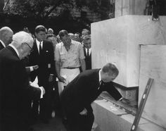 a group of men standing around a white box with writing on it and people looking at it