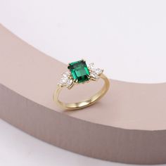 an emerald and diamond ring sitting on top of a table