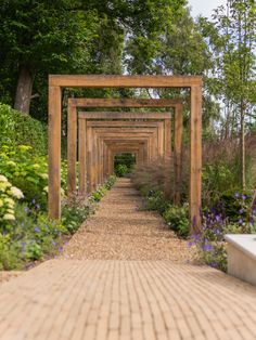 a wooden arch in the middle of a garden with purple flowers and greenery on either side