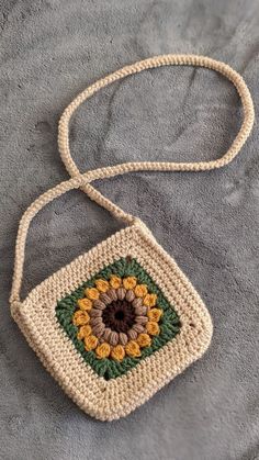 a crocheted bag with a flower on the front and side, sitting on a gray blanket