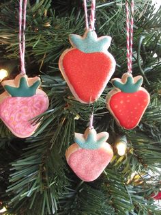 three ornaments hanging from a christmas tree with lights on the top one is pink, green and red