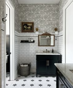 a bathroom with black and white tile flooring and wallpaper, along with a large mirror above the sink