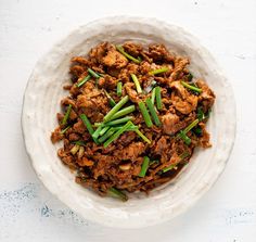 a white bowl filled with meat and green onions