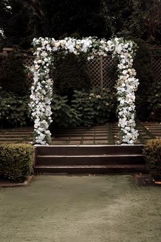 an outdoor wedding ceremony with white flowers and greenery on the back wall, along with steps leading up to it