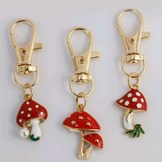 three red and white mushrooms are attached to gold colored metal clips with green leaves on them