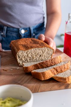 a person holding a loaf of bread on top of a wooden cutting board