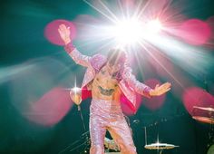 the man is dancing on stage with his hands in the air and lights behind him