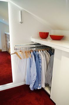 an open closet with shirts hanging on the rails and bowls sitting on top of them