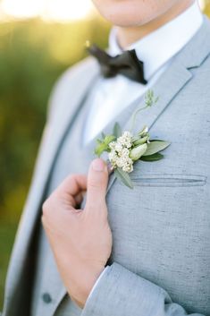 a man in a suit and bow tie is holding onto his boutonniere