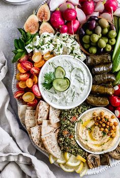 a platter filled with hummus, olives, cucumbers and other foods