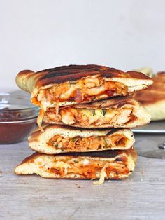 a stack of grilled sandwiches sitting on top of a wooden table next to a bowl of sauce