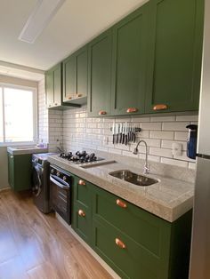 a kitchen with green cabinets and white tile backsplash, stainless steel appliances and wood flooring