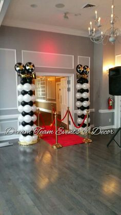 an entrance to a party with black and white balloons, red carpet and gold barriers