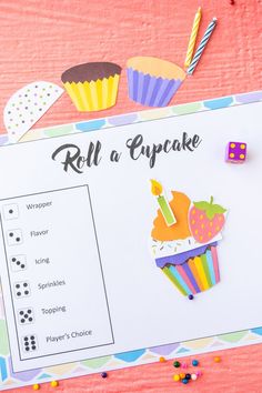 a roll a cupcake game is shown on a pink table with colorful paper decorations