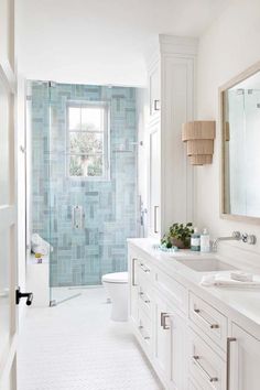 a white bathroom with blue tiles on the shower wall and vanity, along with two sinks