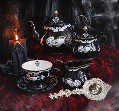 black and white porcelain tea set with candle on red velvet tablecloth in front of dark background