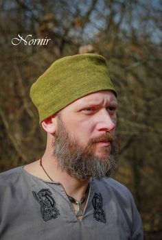 a man with a beard wearing a green knitted hat and looking off to the side