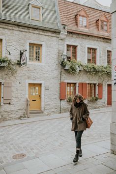 a woman is walking down the street in front of some old stone buildings with red shutters