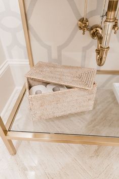 a glass table topped with a basket filled with toilet paper next to a light fixture