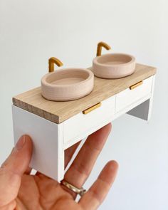 a hand holding a miniature model of two bowls on top of a white countertop