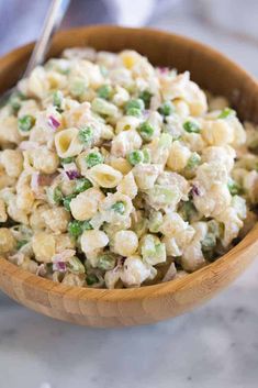 a wooden bowl filled with macaroni salad on top of a marble countertop