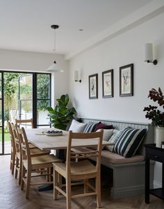 the dining room table is surrounded by wooden chairs and benches with cushions on them, along with potted plants