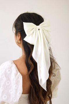 a woman with long hair wearing a large white bow in her hair, looking off to the side