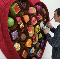 a man is painting the inside of a heart shaped chocolate display with candy and candies