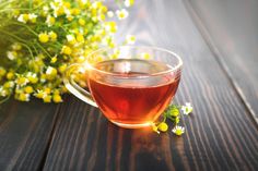 a cup of tea sitting on top of a wooden table next to wildflowers