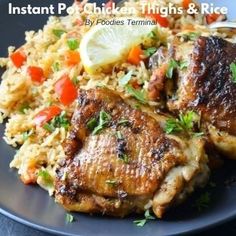 chicken thighs and rice on a black plate with lemon wedges, carrots and parsley