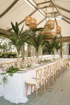 a long table set up with white linens and greenery