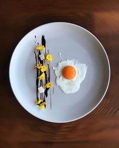 an egg is sitting on top of a white plate with chocolate sauce and yellow flowers