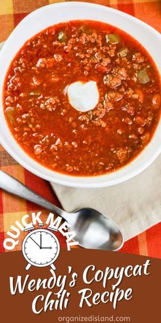 a white bowl filled with chili next to a spoon and napkin on top of a checkered table cloth